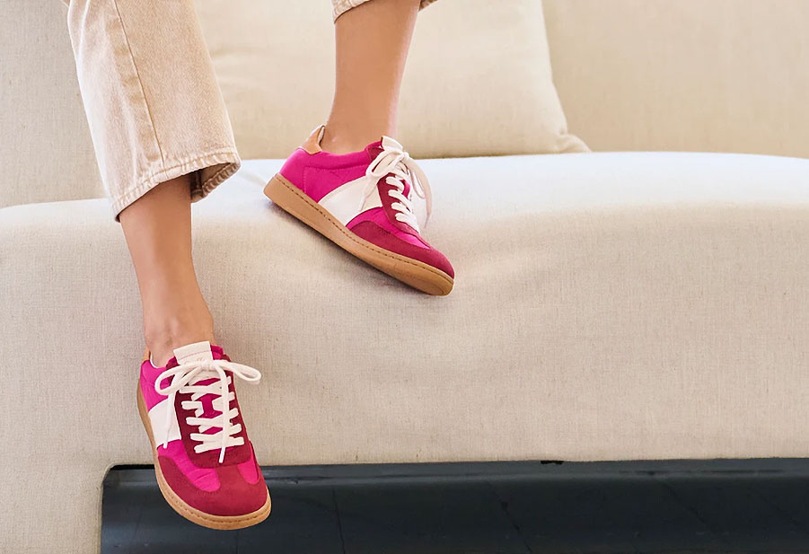 Woman wearing the Ruby sneaker in red sitting on a couch.